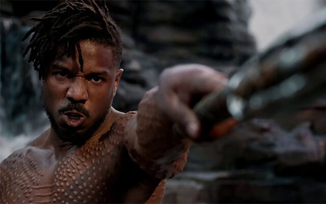 Killmonger empunhando uma arma com expressão intensa em cena do filme Pantera Negra.