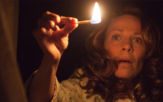 Mulher assustada segurando um fósforo aceso em uma cena escura do filme Invocação do Mal
